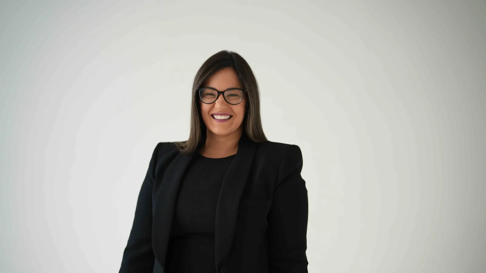 Dr. Andi-Jean Miro smiling in a black suit against a light studio backdrop