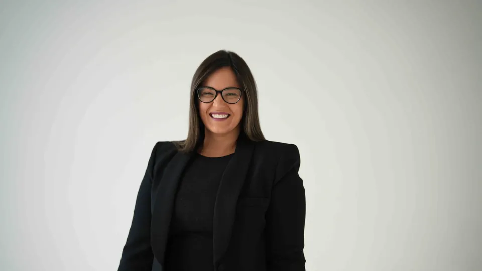 Dr. Andi-Jean Miro smiling in a black suit against a light studio backdrop