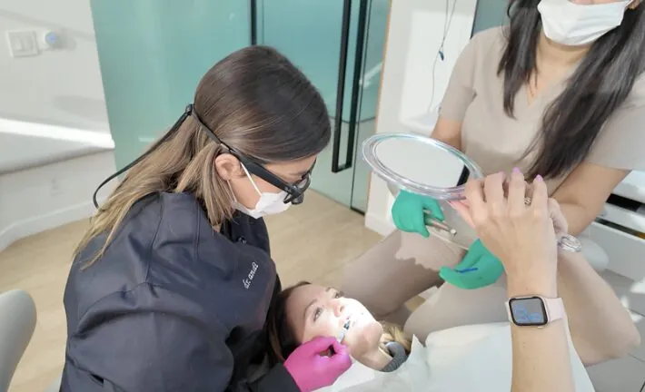 Dr. Andi-Jean Miro evaluating a patient's smile chairside while the patient watches in a hand mirror