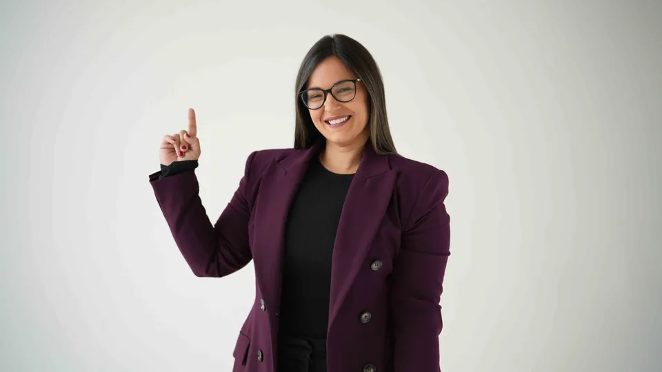 Dr. Andi-Jean Miro in a plum blazer, smiling and raising one finger against a light studio backdrop